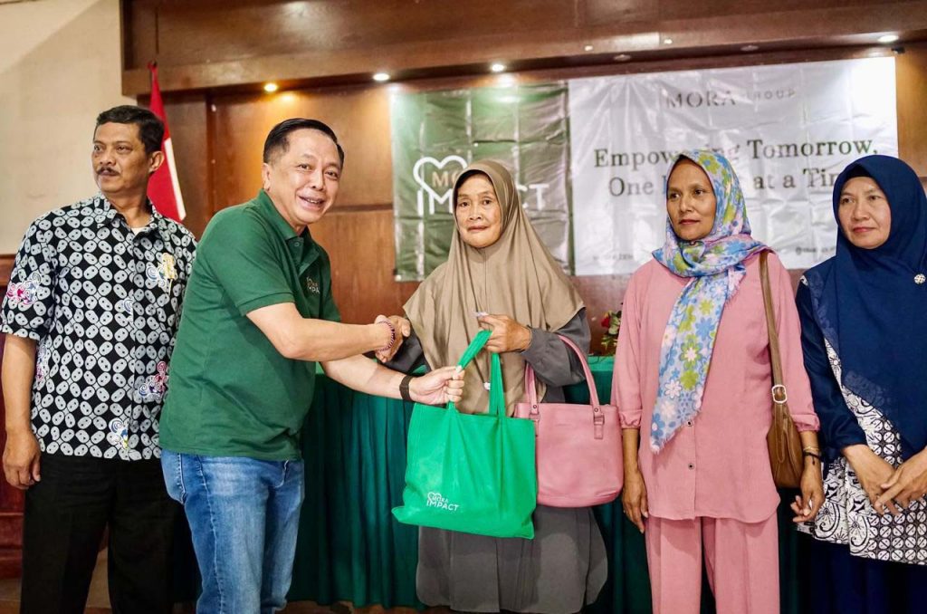 Founder & CEO MORA Group, Andhy Irawan, memberikan goodybag pada lansia di kegiatan tes kesehatan gratis MORA Impact bagi lansia di Kantor Desa Pesanggrahan, Kota Batu, Jumat (19/12/2025).